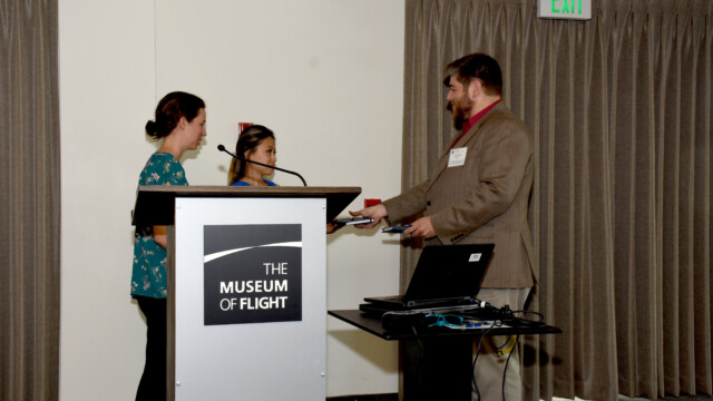 Karine Chen and Hannah Rota, University of Washington Students, are being thanked by Kevin Welch, Event Chairman, for a presentation about their flight test project to show how small unmanned vehicles can perform position estimation in a GPS-degraded environment. They gave an overview of their project and results, and included several entertaining videos of their testing, which was made all the more challenging by the wind conditions at their test site.