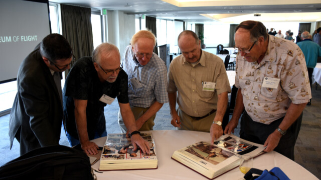 During lunch, Symposium attendees look at scrapbooks covering several decades of John Whitworth's career at Boeing. From left to right: Darren McDonald, Bob Armstrong, Dave Jones, John Whitworth, Henry Stahl.