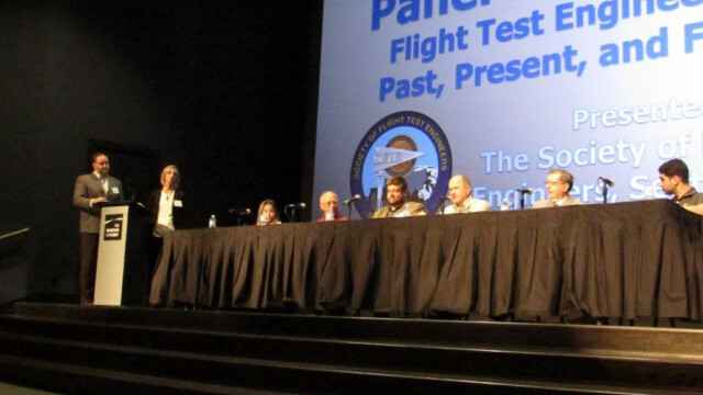 The Public Panel Discussion on Saturday. Topics covered by the panelists, who came from diverse backgrounds, included descriptions of how they got into flight testing, stories of things that happened during flight test, and comparisons of the various roles in a flight test program. The panel also took questions from the audience. Moderators standing on the left are Noah Aaron and Jennifer Boyles. Panelists seated from left to right: Karine Chen, UW graduating Senior in Aerospace Engineering; Leon Robert, Boeing Test Pilot, retired; Kevin Welch, Boeing Flight Test Engineer; John Whitworth, Boeing Flight Test Engineer and Manager, retired; Lee Eccles, Boeing Data Systems Architect, retired; Ramy Mourad, Boeing Flight Test Program Manager and former Eclipse Flight Test Engineer.